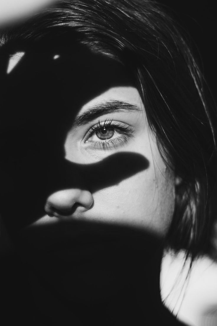 A single softly lit eye emerging from dramatic shadow — OMNIA lash and brow artistry
